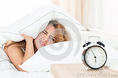 Sleepy girl looking at alarm clock and trying to hide under the Stock Photo