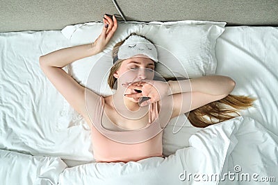 Sleepy yawning young female lying in white bed on pillow, top view Stock Photo