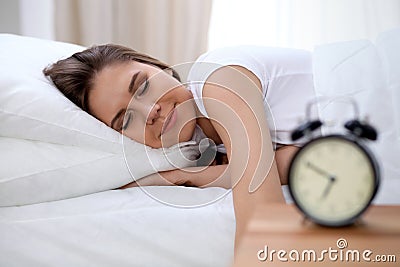 Sleepy young brunette woman stretching hand to ringing alarm willing turn it off. Early wake up, not getting enough Stock Photo