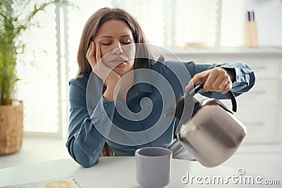 Sleepy young woman pouring coffee into cup at home in morning Stock Photo