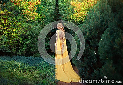 Slender beauty in elegant bright dress with stretching trains goes to thick of magical garden, golden elf princess with Stock Photo