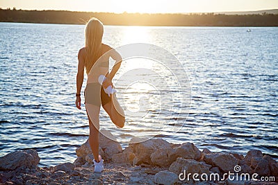 Slender fit woman on rocky beach stretching after workout Stock Photo