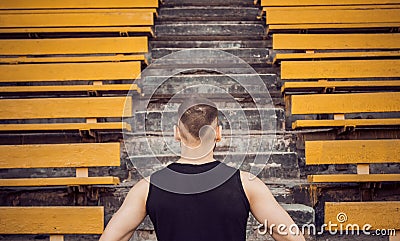 A slender young man in black sportswear stands in front of the stairs stadium stands. ready for action, step to victory, challenge Stock Photo