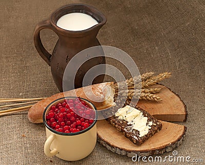 A slice of buttered bread on a wooden board, a crock of milk, a metal cup of red currants and mature ears Stock Photo