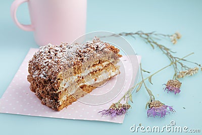 Slice of cake with icing on duck egg blue background with dried flowers and pink cup of milk Stock Photo