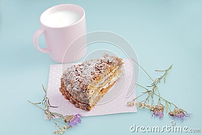 Slice of cake with icing on duck egg blue background with dried flowers and pink cup of milk Stock Photo