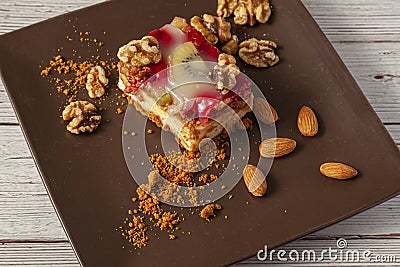 A slice of fruit cheesecake served on a brown porcelain plate with walnuts and almonds. Stock Photo