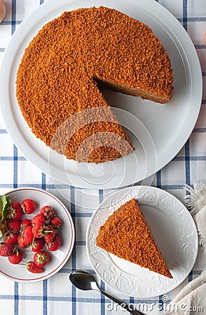 A slice of homemade multilayer honey cake. Orange color. On a white plate. View from above. Testura. Nearby are berries, apples, Stock Photo