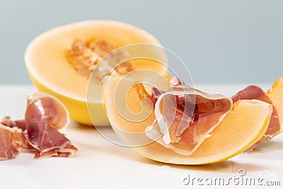 Slice of melon with cured ham on top next to some cured ham slices and ahalf melon behind Stock Photo