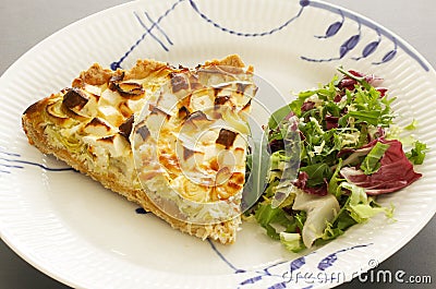 A slice of quiche with leek and feta or goats cheese on a plate with crispy leaf green salad. Vegetarian food image close up Stock Photo