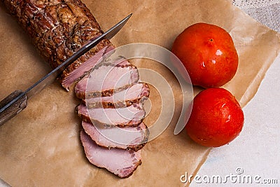 Slice smoked meat or ham, knife and two tomatoes on brown packing paper.. Stock Photo