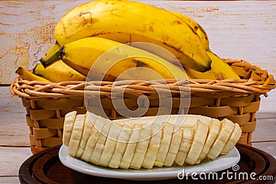 Sliced banana on a white plate on a wooden tray with a wicker basket with bananas in the background Stock Photo