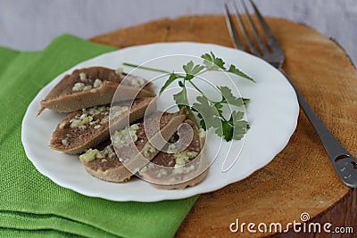 Sliced boiled beef tongue on white plate green napkin and wooden table with parsley garlic sauce, horizontal, copy space Stock Photo