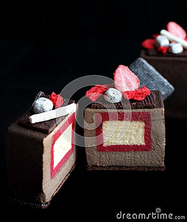 Sliced dark chocolate textured cube dessert with strawberry and vanilla insertion, silver cookie decorations and red Stock Photo