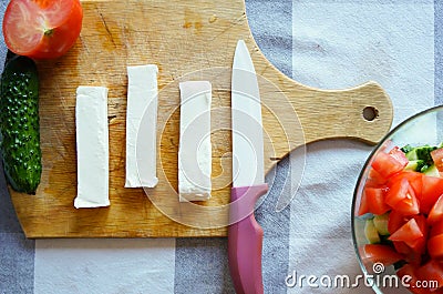 Sliced feta cheese cheese on a wooden board with vegetables and a knife Stock Photo
