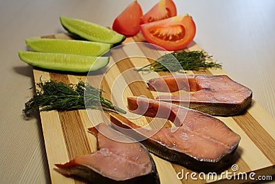 Sliced fish with cucumber and tomato and dill on a wooden board. Stock Photo