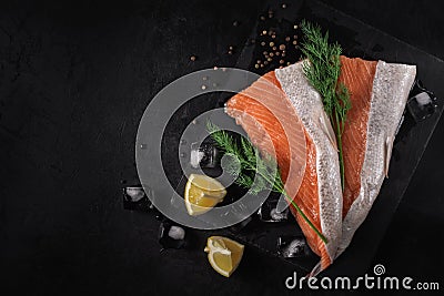 Sliced fresh raw salmon lying on a stone cutting board with lemon wedges, dill, spices and ice cubes on a black textured concrete Stock Photo