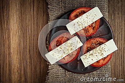 sliced fresh tomatoes under soft cheese with mediterranean spices on a clay plate on a burlap napkin on an old textured wooden Stock Photo