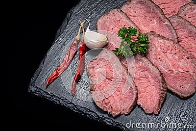 Sliced Grass Fed Corn Roast Beef garnished with Garlic, Fresh Curly Parsley and dried Red Chile De Arbol Peppers Stock Photo