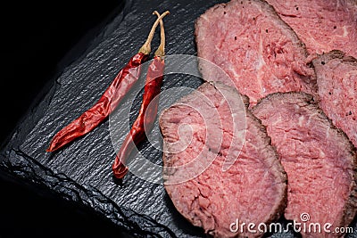 Sliced Grass Fed Juicy Corn Roast Beef garnished with dried Red Chile De Arbol Pepper on black natural stone Stock Photo