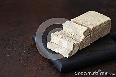 Sliced halva on a wooden tray on a brown background. Oriental sweets Stock Photo