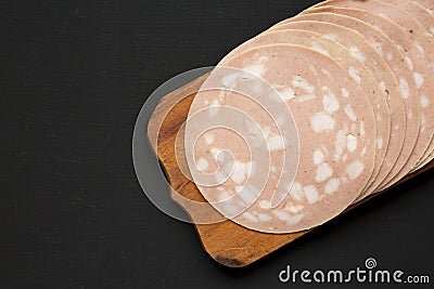 Sliced Mortadella Bologna Meat on a rustic wooden board over black background, top view. Flat lay, from above, overhead. Space for Stock Photo