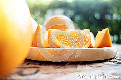 Sliced Orange on Wooden Plate. Fresh Juicy Fruit in Summer. Selective Focus. Blurred Tree with Lens Flare Stock Photo