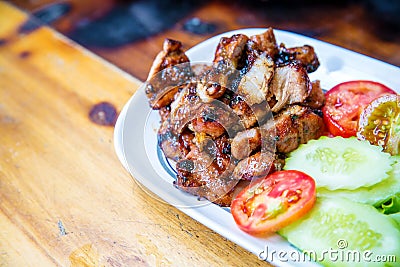 Sliced pork roasted thai style with green leaves salad on rustic plate with cutlery. Stock Photo