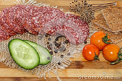 Sliced smoked sausage with bacon and sliced green cucumber and three red tomatoes cherry and pieces of rye bread crumbs Stock Photo