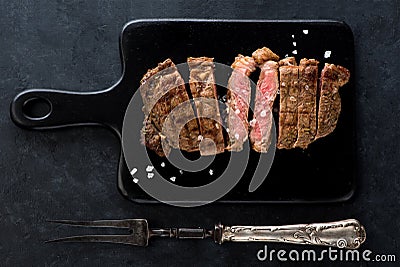 Slices beef Steak Ribeye on a black cutting board and meat fork Stock Photo