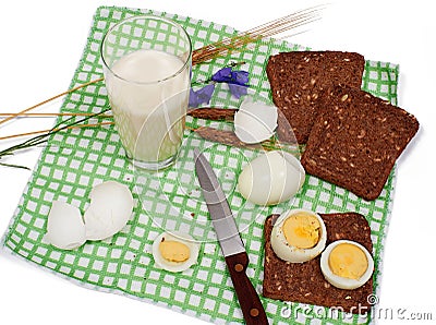 Slices of bread with eggs, glass of milk, rye and bluebell flower on checkered table-napkin Stock Photo