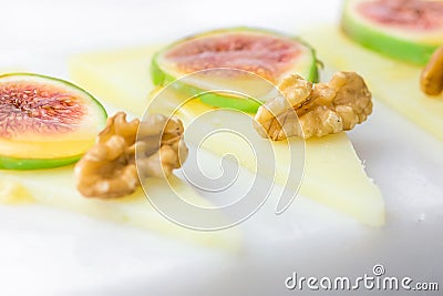 Slices of cured semi-hard Spanish goat cheese with walnuts, ripe figs drizzled with honey on white marble serving board. Appetizer Stock Photo