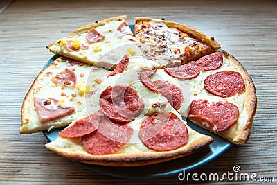 Slices of different pizza with bacon, pepperoni sausages, mushrooms and cheese on a plate and a wooden background Stock Photo