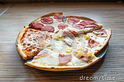 Slices of different pizza with bacon, pepperoni sausages, mushrooms and cheese on a plate and a wooden background Stock Photo