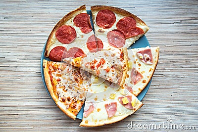 Slices of different pizza with bacon, pepperoni sausages, mushrooms and cheese on a plate and a wooden background. Top view Stock Photo