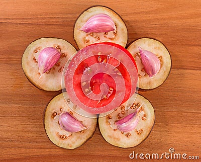 Slices of eggplant with cloves of garlic and a half of tomato on a wooden board surface Stock Photo