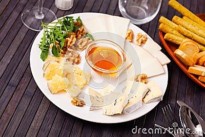 Slices of four cheeses on plate with honey, walnuts and arugula Stock Photo