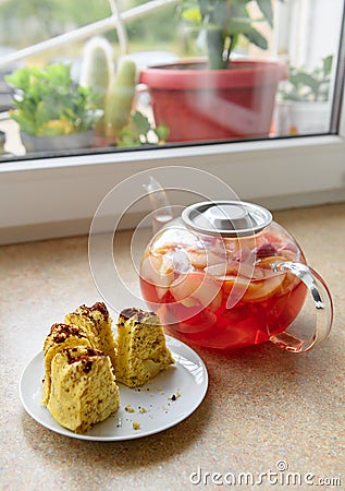 Slices of homemade cake on a plate and glass teapot with stewed fruits - apples, plums and strawberries on the windowsill, concept Stock Photo