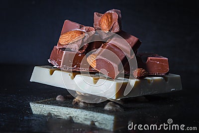 Slices of milk chocolate with almonds and tiles of white chocolate with hazelnuts on an old dark metallic background Stock Photo