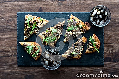 Slices of mushroom beef flatbread pizza on slate board with glasses of cola. Stock Photo