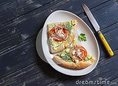 Slices pizza with zucchini, tomatoes, onions and feta cheese on a light ceramic plate on dark wooden background. Stock Photo