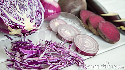 Slices of purple vegetables on wooden background - eggplant, beets, basil, onion, cabbage Stock Photo