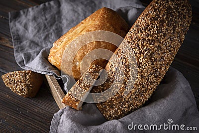 Rye grain bread in a basket with a napkin on a dark wooden background, wheat loaf, ciabatta, close-up, top view Stock Photo