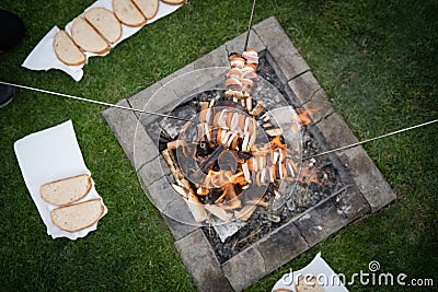 Slices of sausage, bacon and onion roasted on bonfire flame in garden Stock Photo