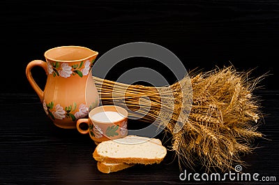 Slices of white bread, a cup of milk and a jug, a sheaf of wheat ears on a black table Stock Photo