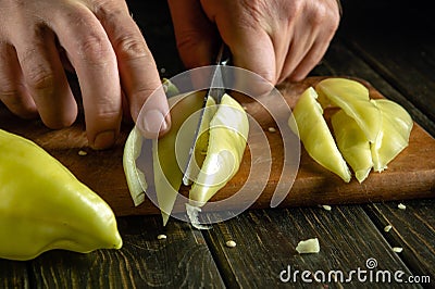 Slicing pepper with a knife in the hand of a cook. The idea of preparing a vegetable diet on the kitchen table at home Stock Photo