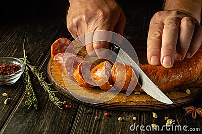 Slicing sausage on a wooden cutting board in the home kitchen by the hands of a cook. The idea of cooking fast food Stock Photo