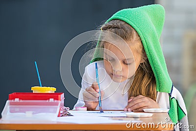 Slightly disheveled girl watercolor paints sitting at the table in the yard Stock Photo