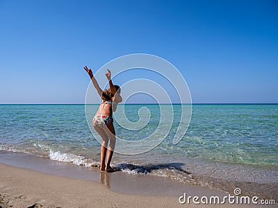 Slim and athletic girl in a colorful bikini ready to jump before a crystal clear water of a beautiful beach Stock Photo