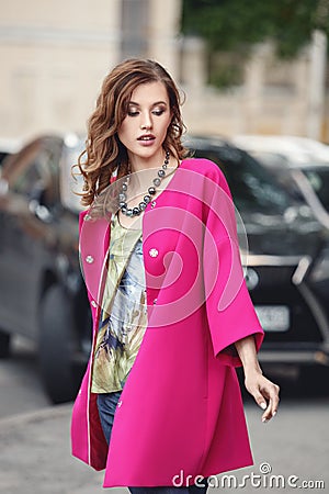 Slim beautiful girl dressed in a stylish summer fuchsia corol coat walks on a city street Stock Photo